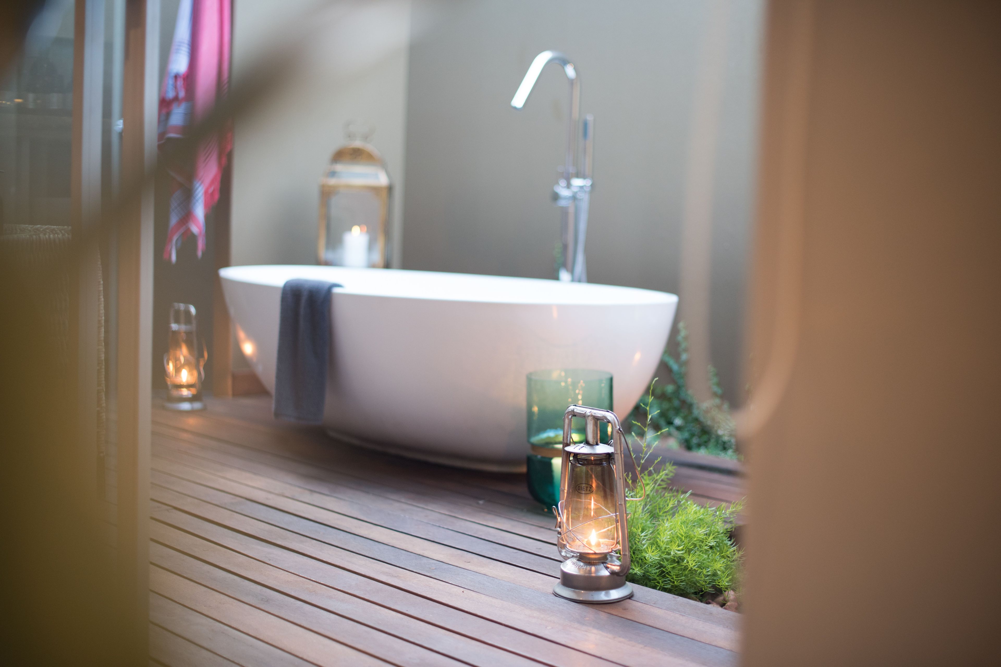 A bathroom with a white bathtub, a modern faucet, and a small lantern on a wooden deck.