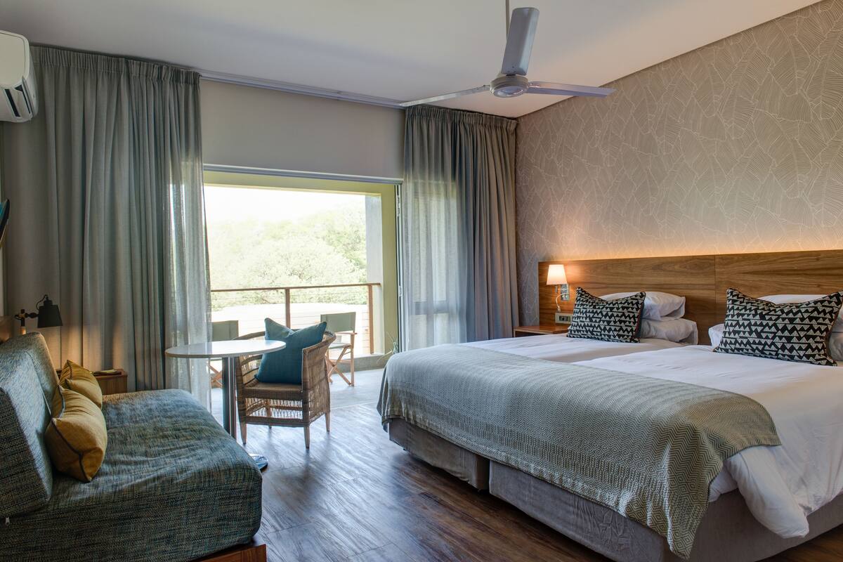 A hotel room with a large bed, a sofa, a dining table, and a ceiling fan.