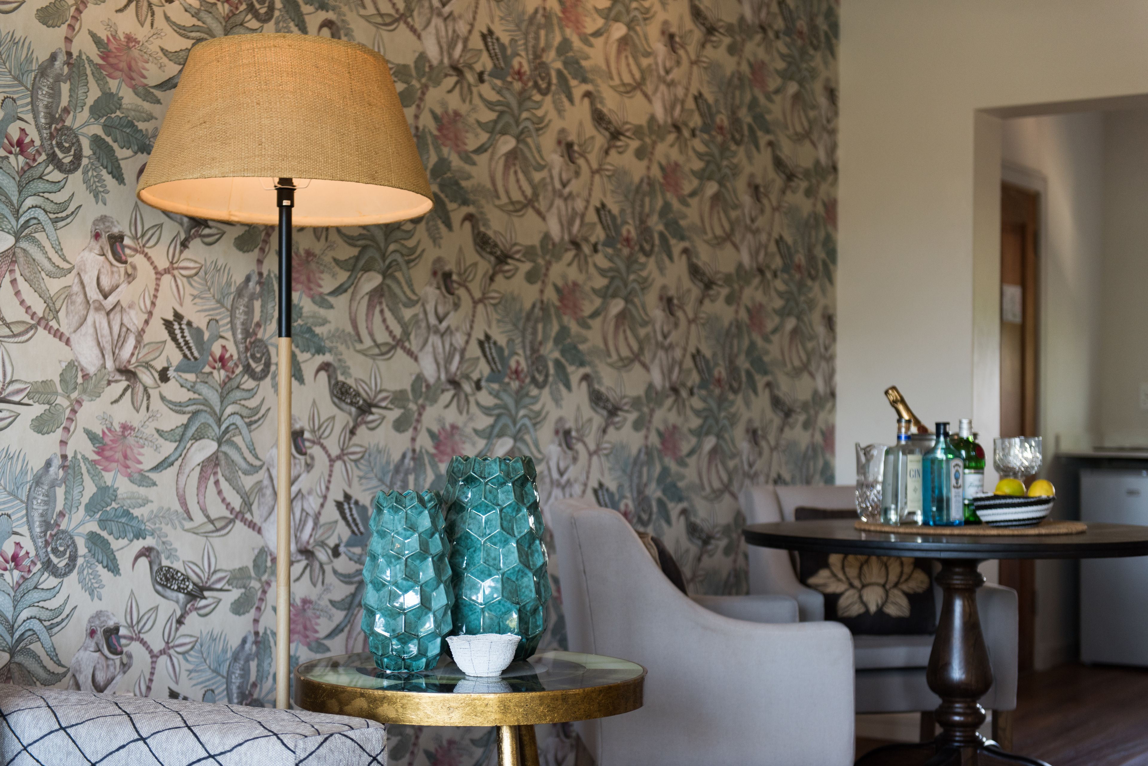 Une pièce avec un papier peint à motifs floraux, une table ronde avec une lampe et un canapé.