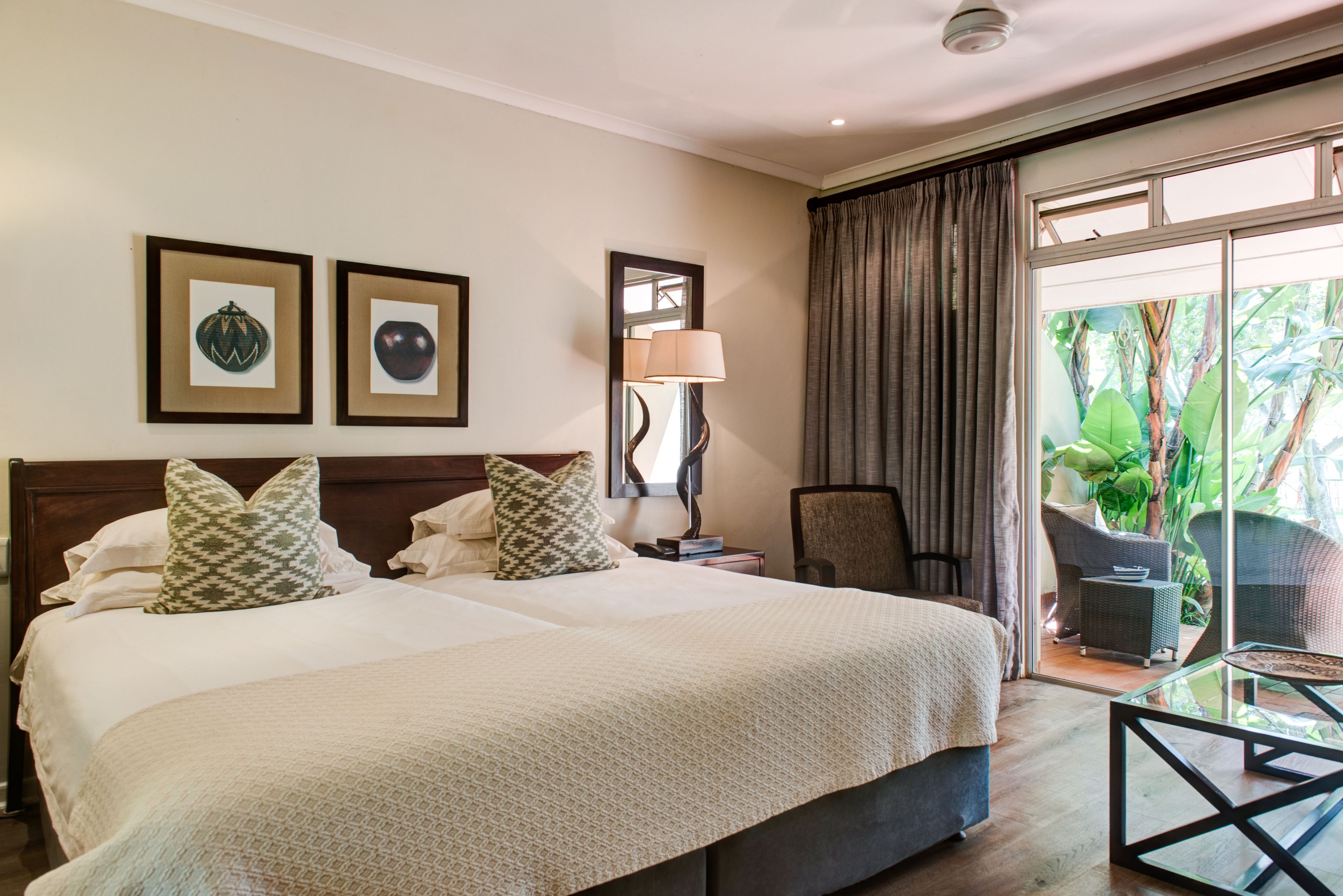 Quarto de hotel com uma cama grande, duas fotos emolduradas na parede, um abajur, uma cadeira e uma mesa de vidro.