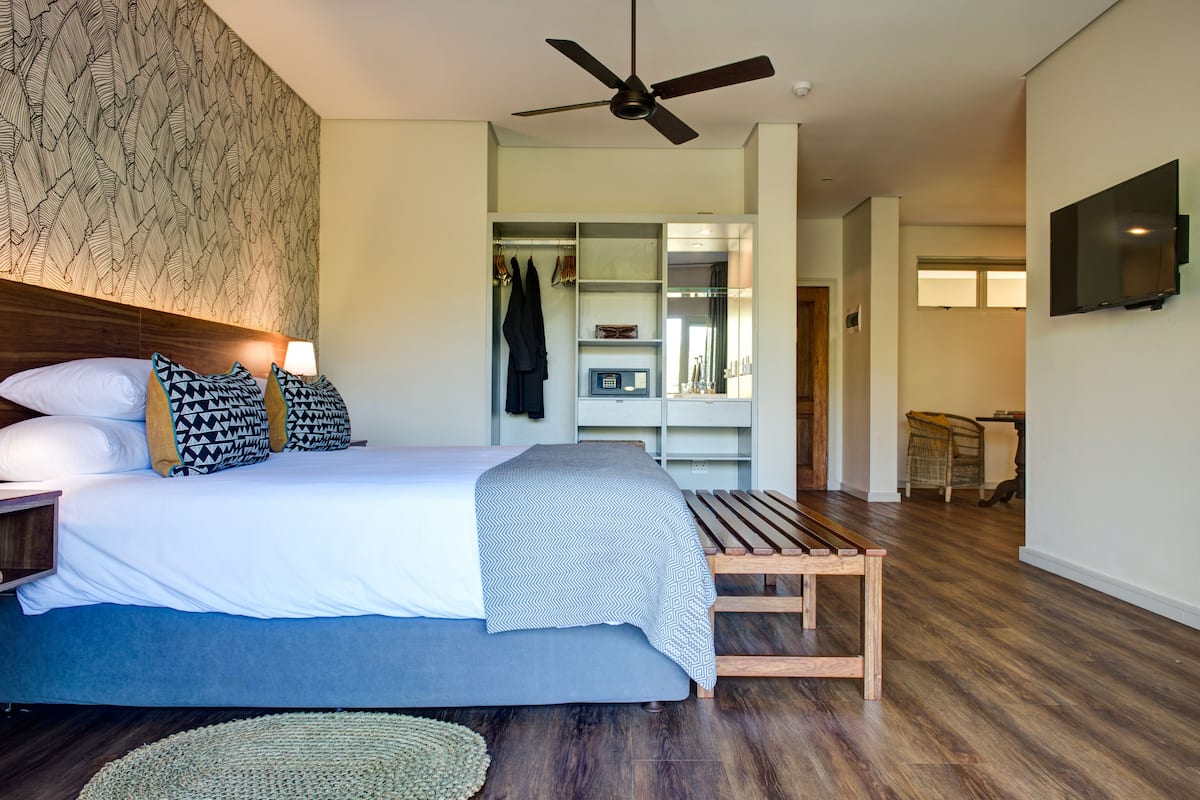 A modern bedroom with a bed, bedside lamps, a ceiling fan, a wooden bench, a closet, and a television on the wall.