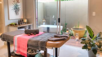 Relax in this serene spa room, featuring a massage table, an outdoor area with a bathtub, and lush greenery.