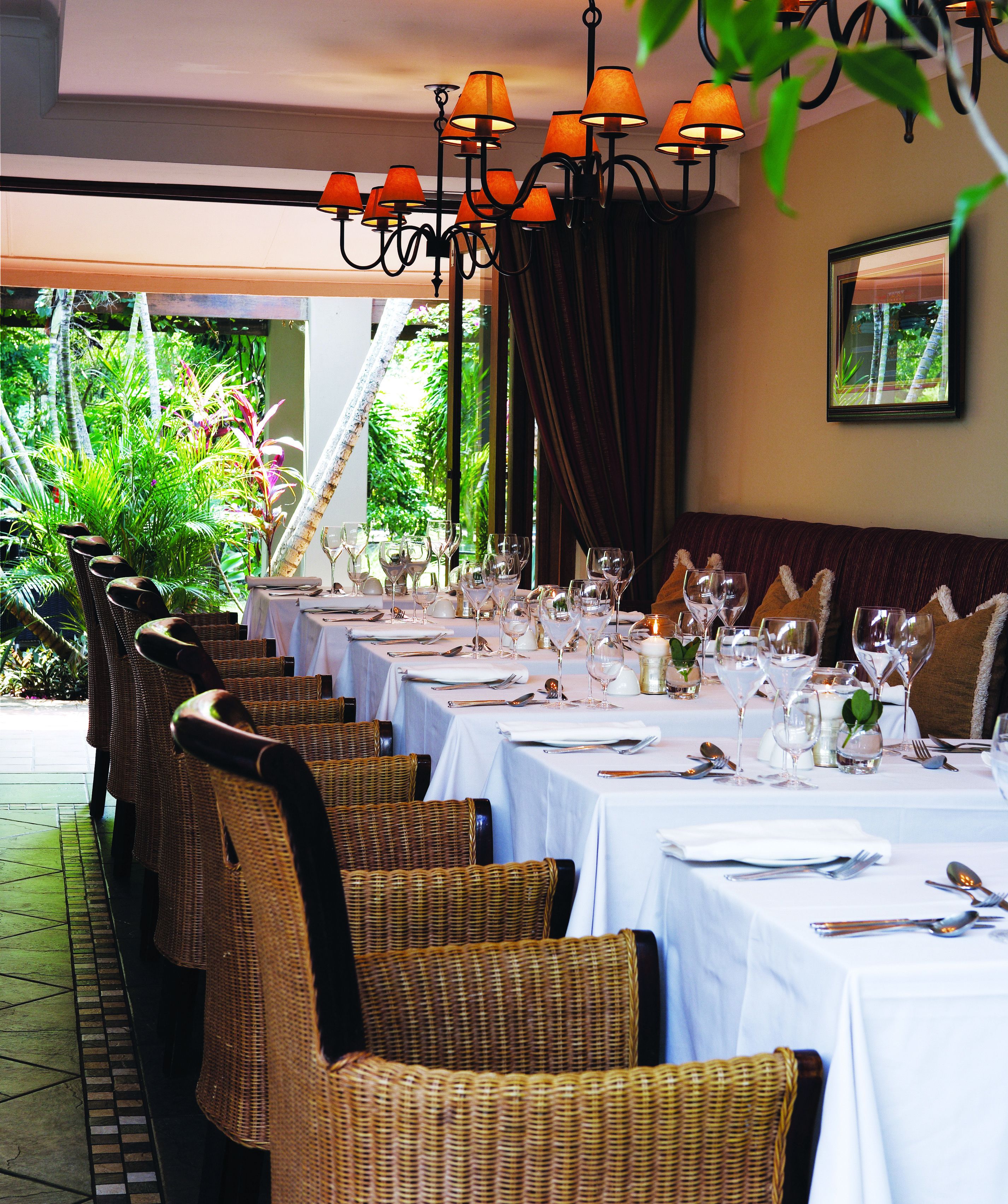 A restaurant with wicker chairs, white tablecloths, and orange lamps.
