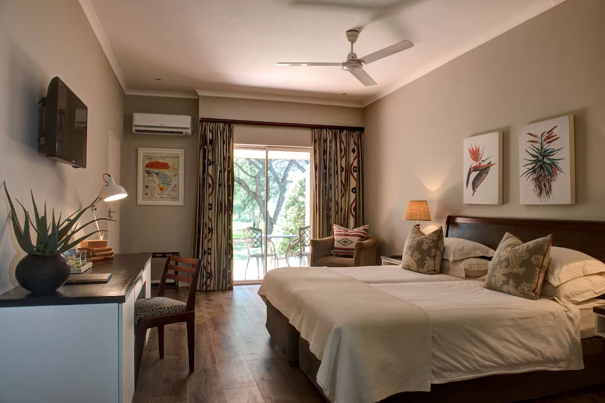 A bedroom with a bed, two bedside tables, a desk, a chair, a ceiling fan, and a window with curtains.