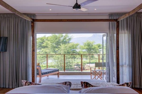 A bedroom with a large bed, a ceiling fan, and a balcony with a view of greenery. - Ghost Mountain Inn (Jozini)