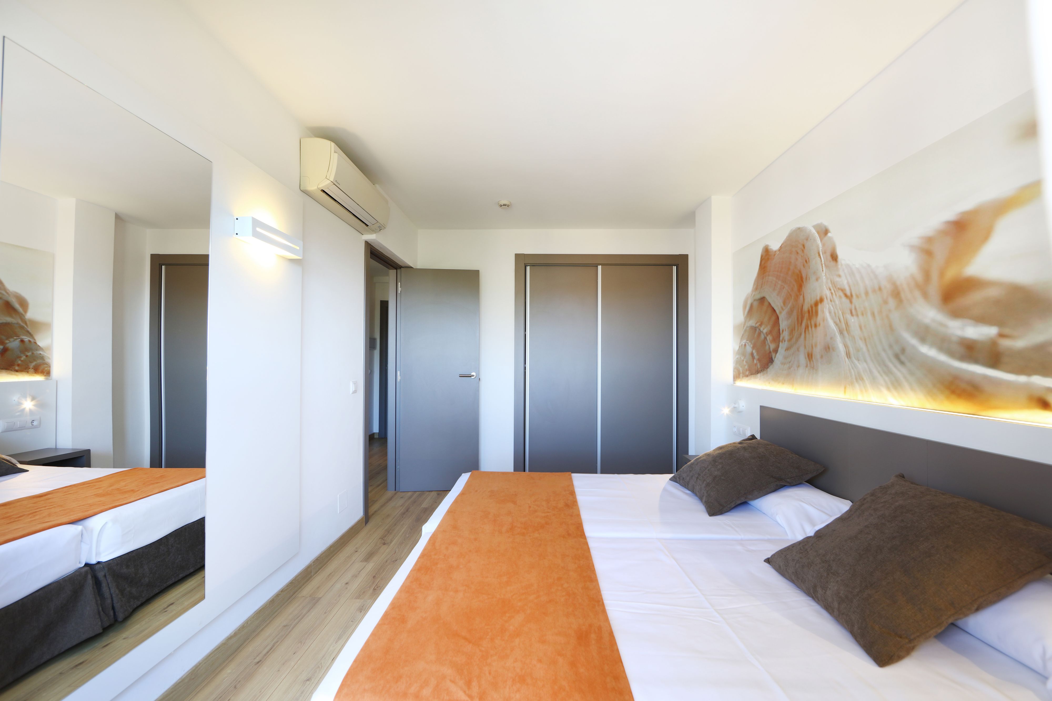 Una habitación de hotel moderna con una cama grande, una mesita de noche, un espejo y un armario.