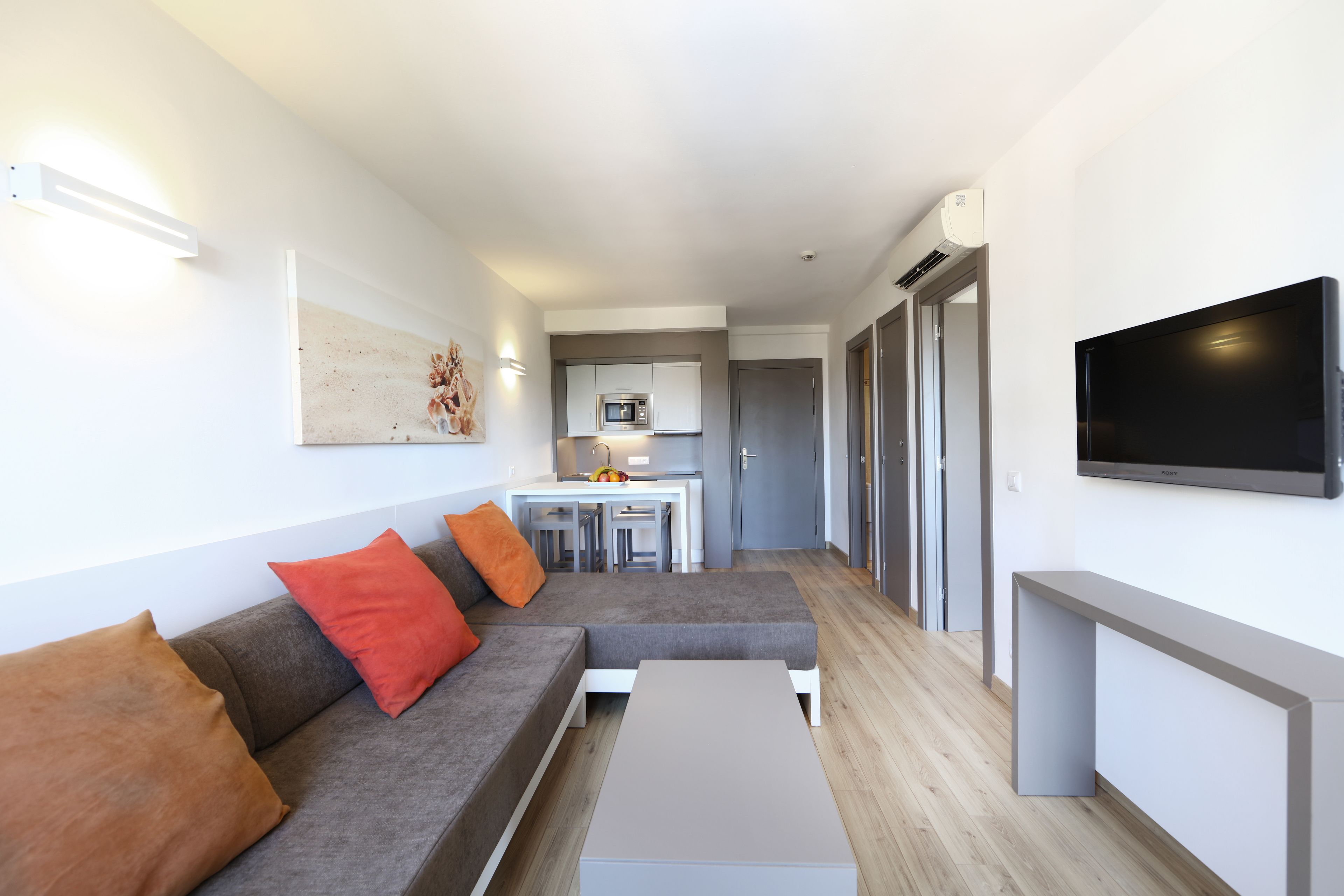 Un salon moderne avec un canapé gris, des coussins orange, une table basse et un téléviseur à écran plat fixé au mur.