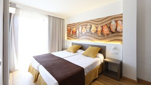 A hotel room with a large bed, two bedside tables, a wall-mounted light, and a window with curtains. - Apartamentos Jade - Adults Only +16 (Palma de Mallorca)