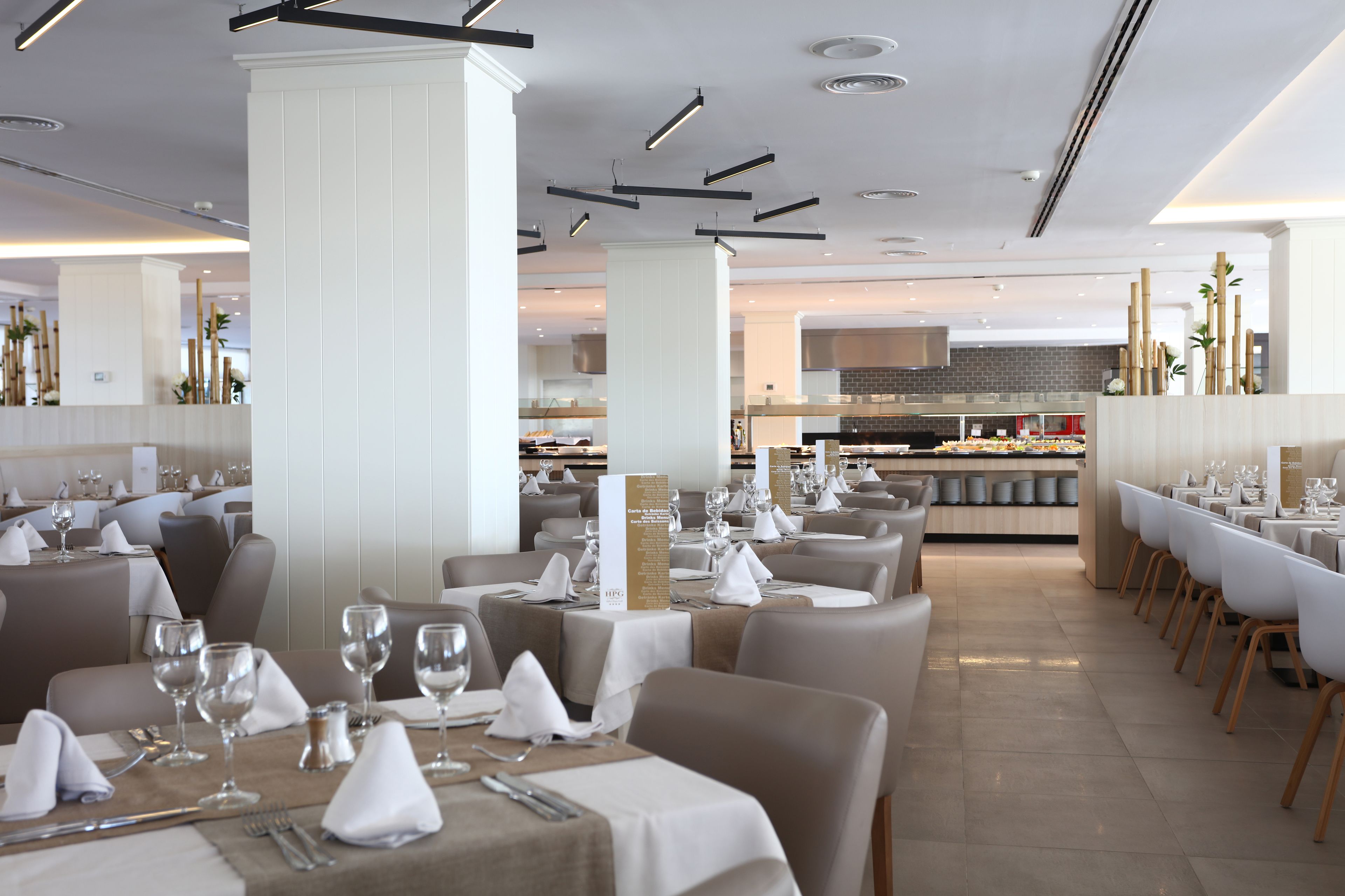 Un restaurante moderno con mesas y sillas ordenadas, una columna central y un área de cocina al fondo.