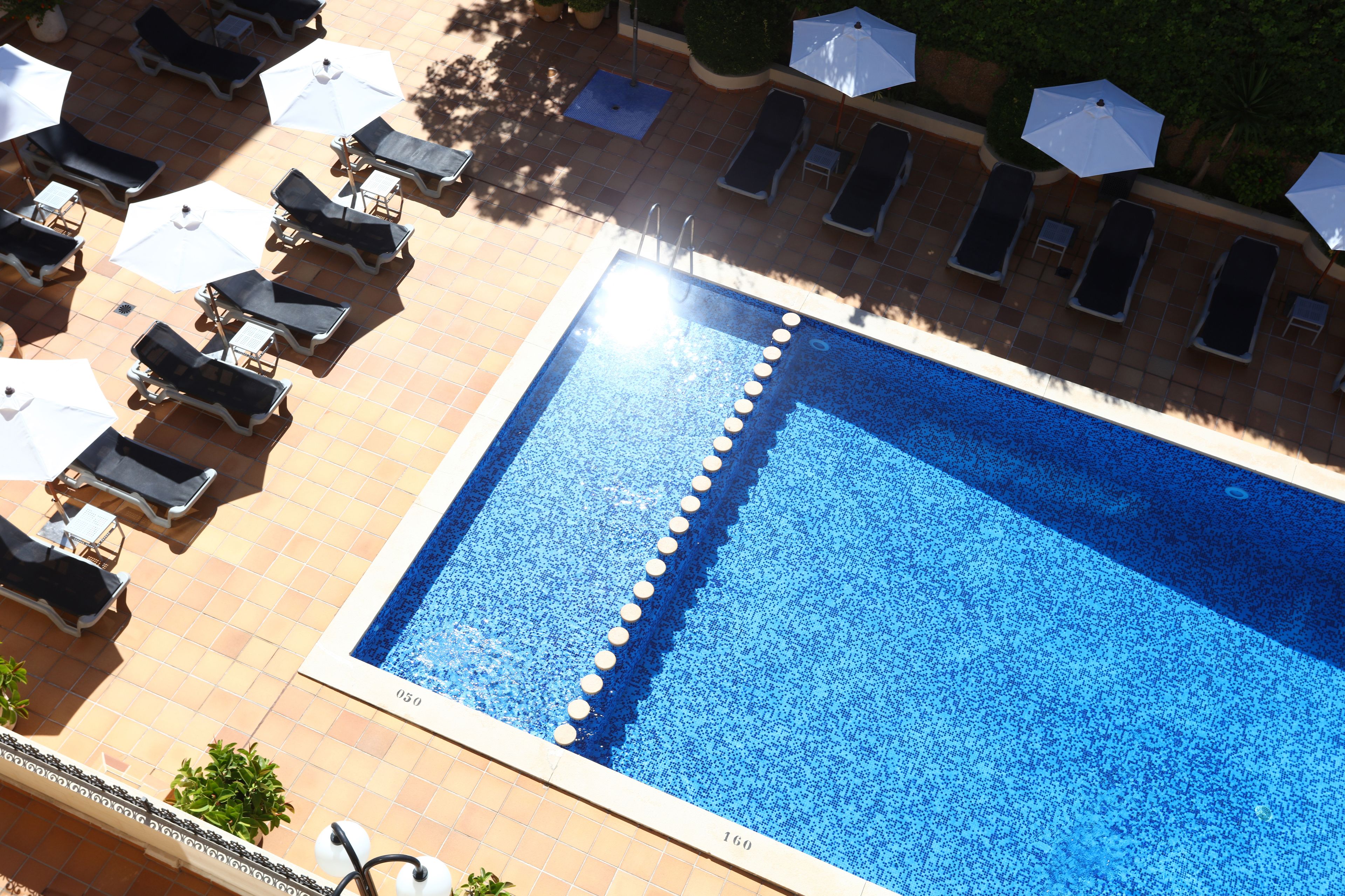 A rooftop pool with sun loungers and umbrellas, surrounded by a tiled deck.