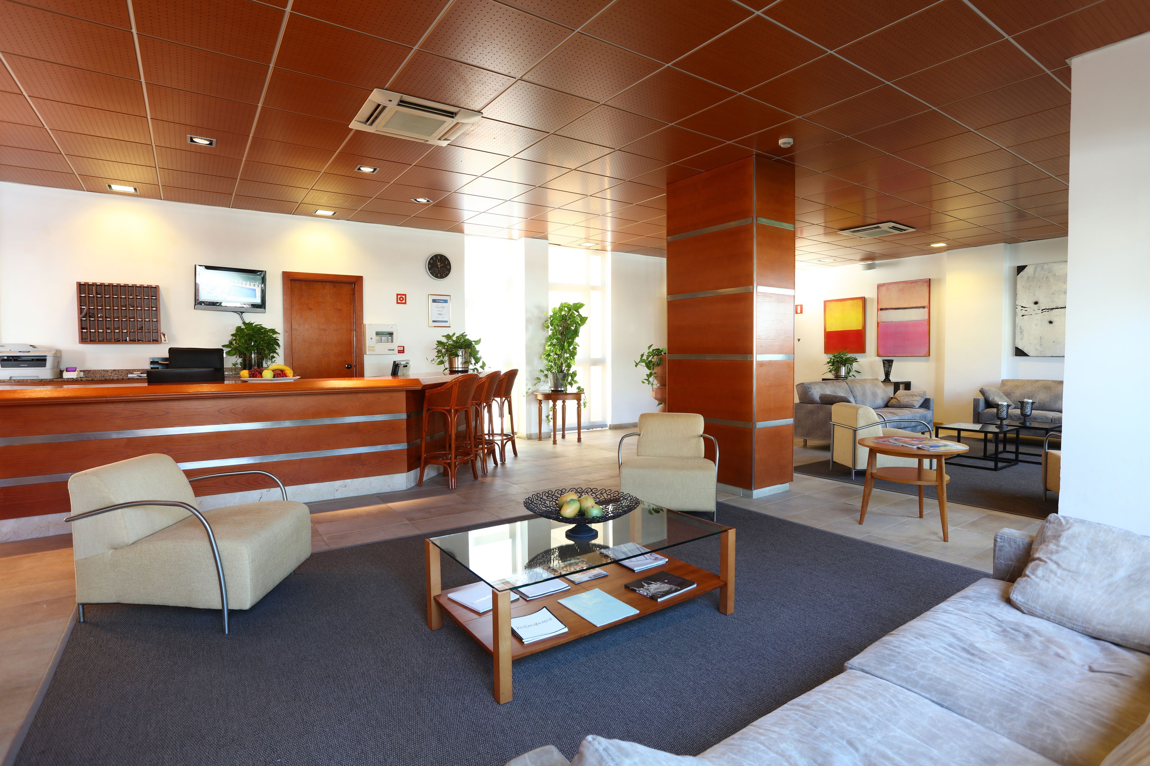 A modern hotel lobby with a reception desk, seating area, and a dining space.