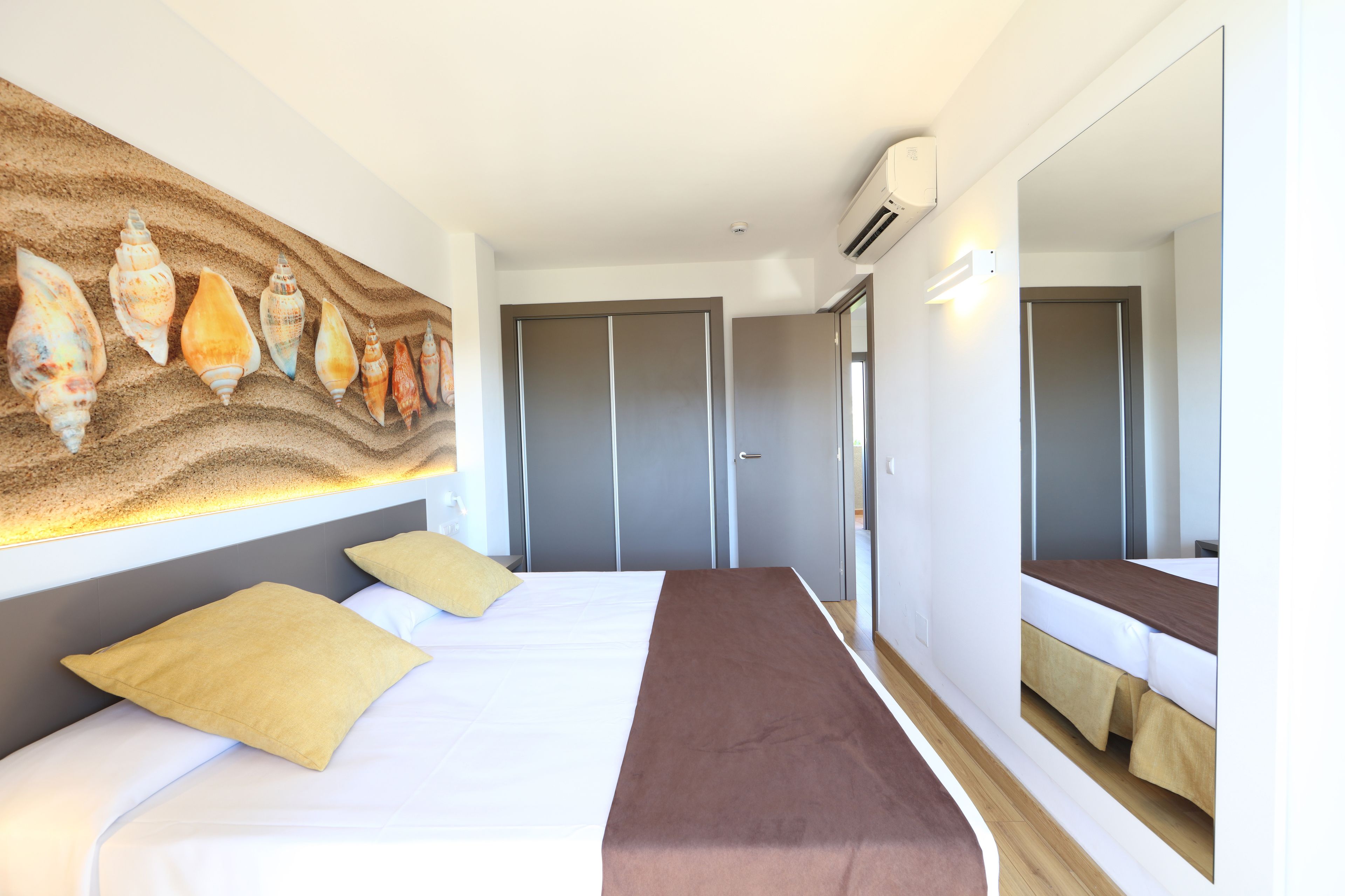 A hotel room with a bed, a wall-mounted artwork of seashells, a wardrobe, and a mirror.