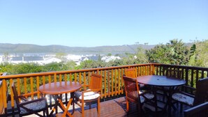 A wooden deck with a table and chairs, overlooking a scenic view of a lake and buildings. - Knysna Manor House (Knysna)