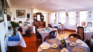 A dining area with multiple tables set for meals, wooden chairs, and a decorative mirror. - Knysna Manor House (Knysna)
