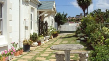 Un edificio blanco con un patio empedrado, plantas en macetas y una mesa de piedra.