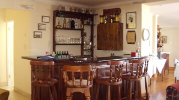 A bar area with wooden stools, a bar counter, and shelves with bottles and glasses.