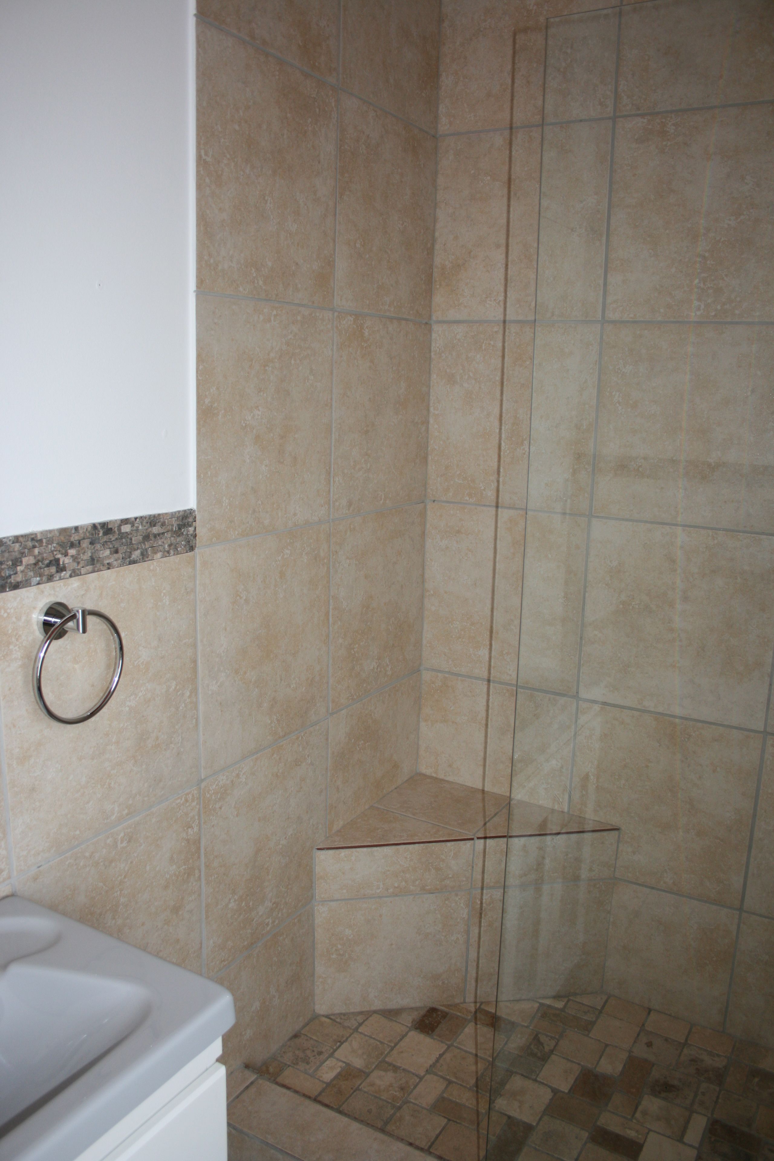 A bathroom with beige tiles, a glass shower enclosure, and a white sink.