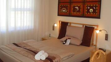 Une chambre d’hôtel avec un grand lit, deux lampes de chevet, une tête de lit, un mur orné d’un motif matelassé et une fenêtre avec des rideaux légers.