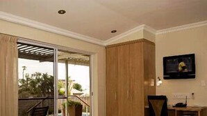 A hotel room with a bed, a desk, a chair, and a view of a pool and palm trees through a sliding glass door. - Hajo's Lodge & Spa (Cape Town)