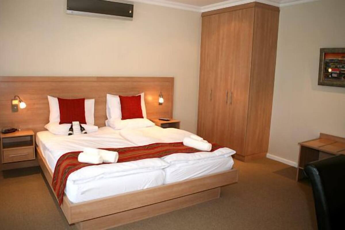 A neatly made bed with white linens and red accents, a wooden headboard, bedside lamps, and a wardrobe.