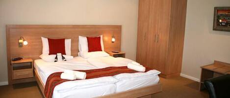Una cama bien hecha con ropa de cama blanca y detalles en rojo, un cabecero de madera, lámparas de noche y un armario.