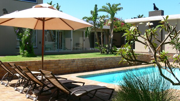 A poolside area with lounge chairs and an umbrella, surrounded by a brick wall and greenery. - Hajo's Lodge & Spa (Cape Town)