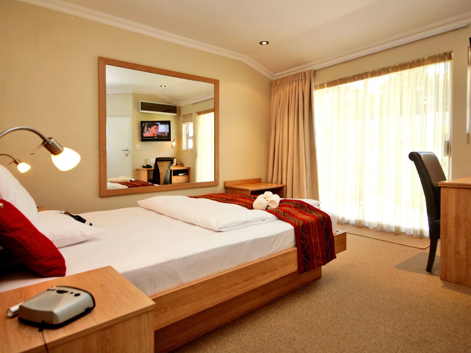 Une chambre d’hôtel avec un lit, un bureau, une chaise, une télévision et un grand miroir.