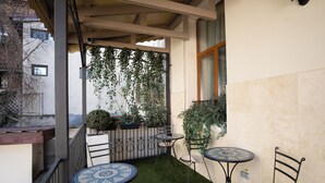 A balcony with artificial grass, two round tables with chairs, and a white fence with plants.
