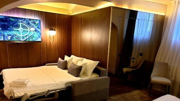A hotel room with a bed, a sofa, a TV, and a mirror.