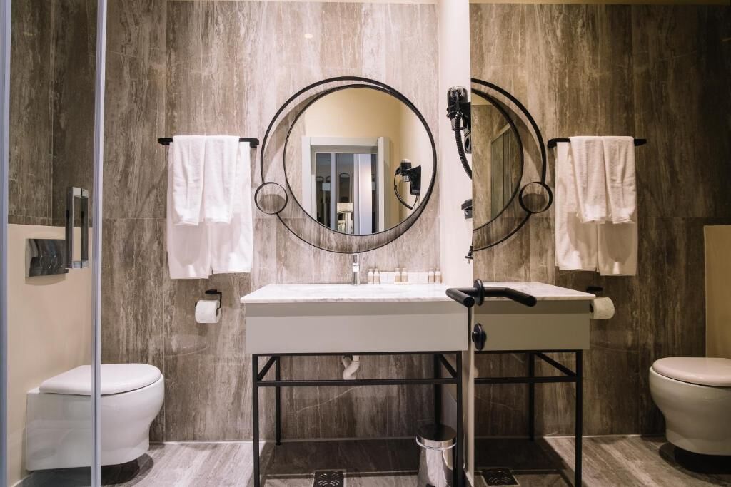 A bathroom with two toilets, a sink with a mirror, and towels hanging on hooks.