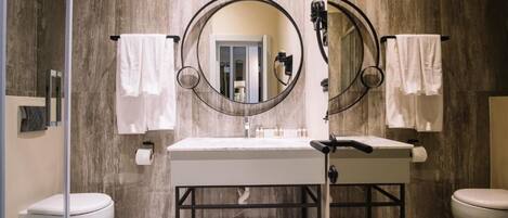 A bathroom with two toilets, a sink with a mirror, and towels hanging on hooks.