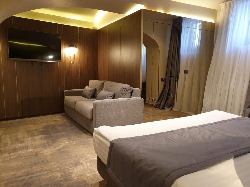 Habitación de hotel con sofá, cama, televisor montado en la pared y cortina.