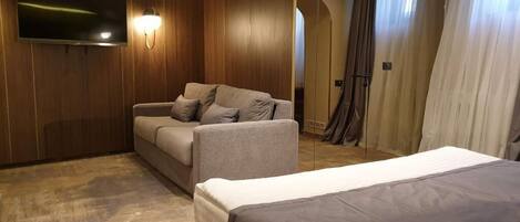 Habitación de hotel con sofá, cama, televisor montado en la pared y cortina.