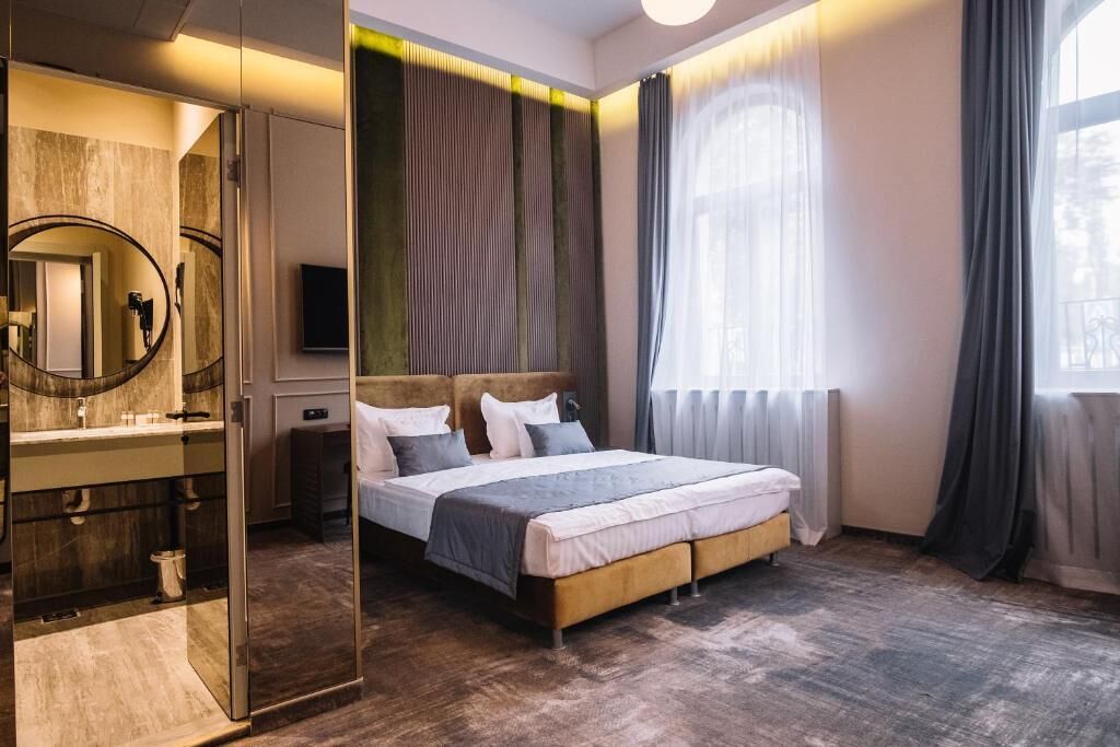 Une chambre à coucher moderne avec un grand lit, un miroir, une coiffeuse et une vue sur l’extérieur.