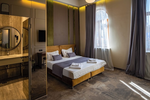 A hotel room with a bed, a mirror, a TV, and a window with curtains.