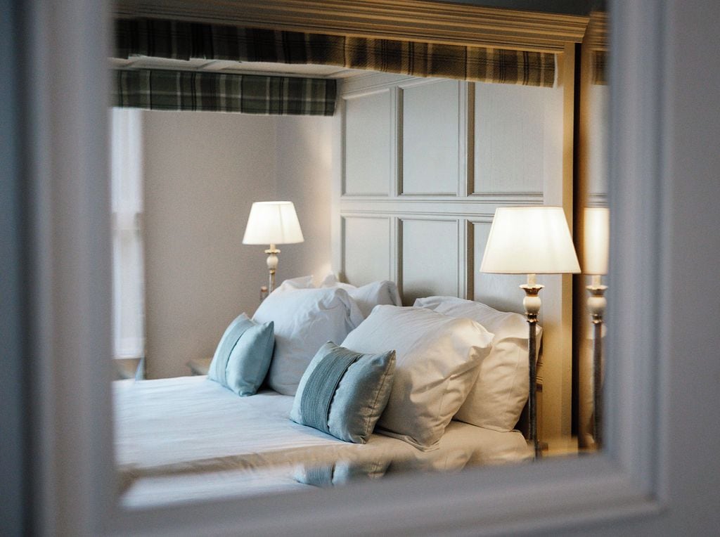 A hotel room with a bed, two bedside lamps, and a headboard with a plaid pattern.