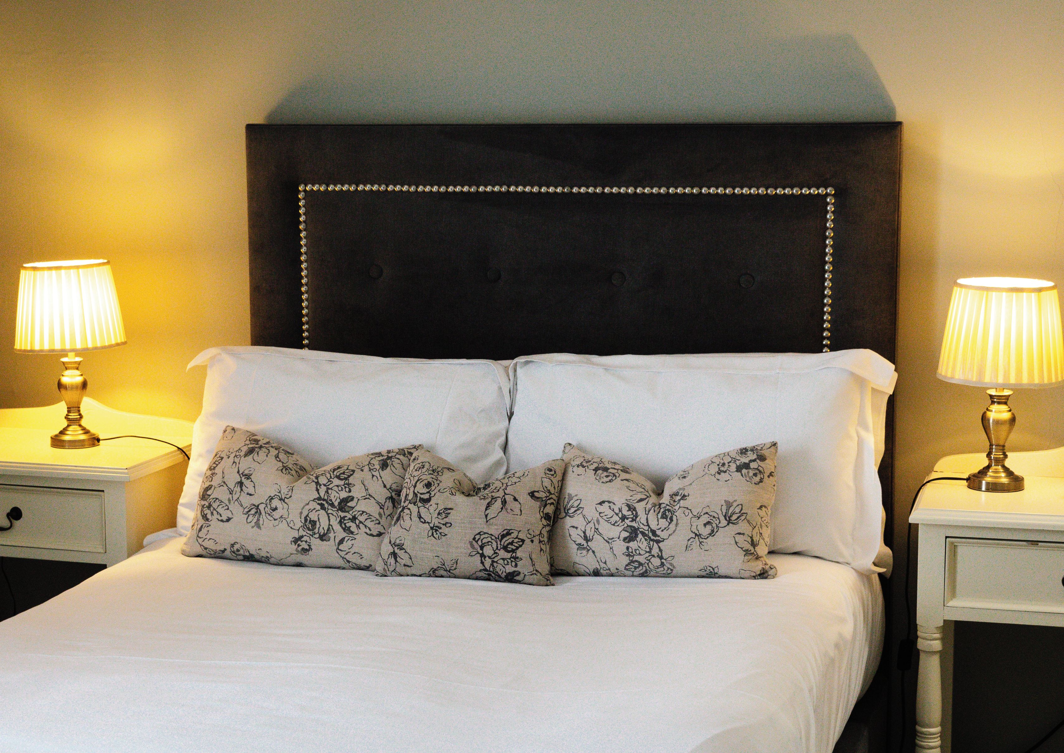 A neatly made bed with floral-patterned pillows, a dark upholstered headboard, and two bedside lamps on white nightstands.