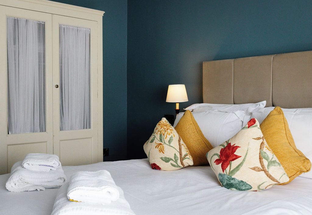 Quarto de hotel com cama, almofadas, luminária, guarda-roupa e toalhas.