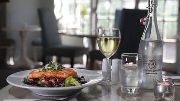 Una mesa de comedor con un plato de comida, una copa de vino blanco, una botella de agua con gas y una vela.