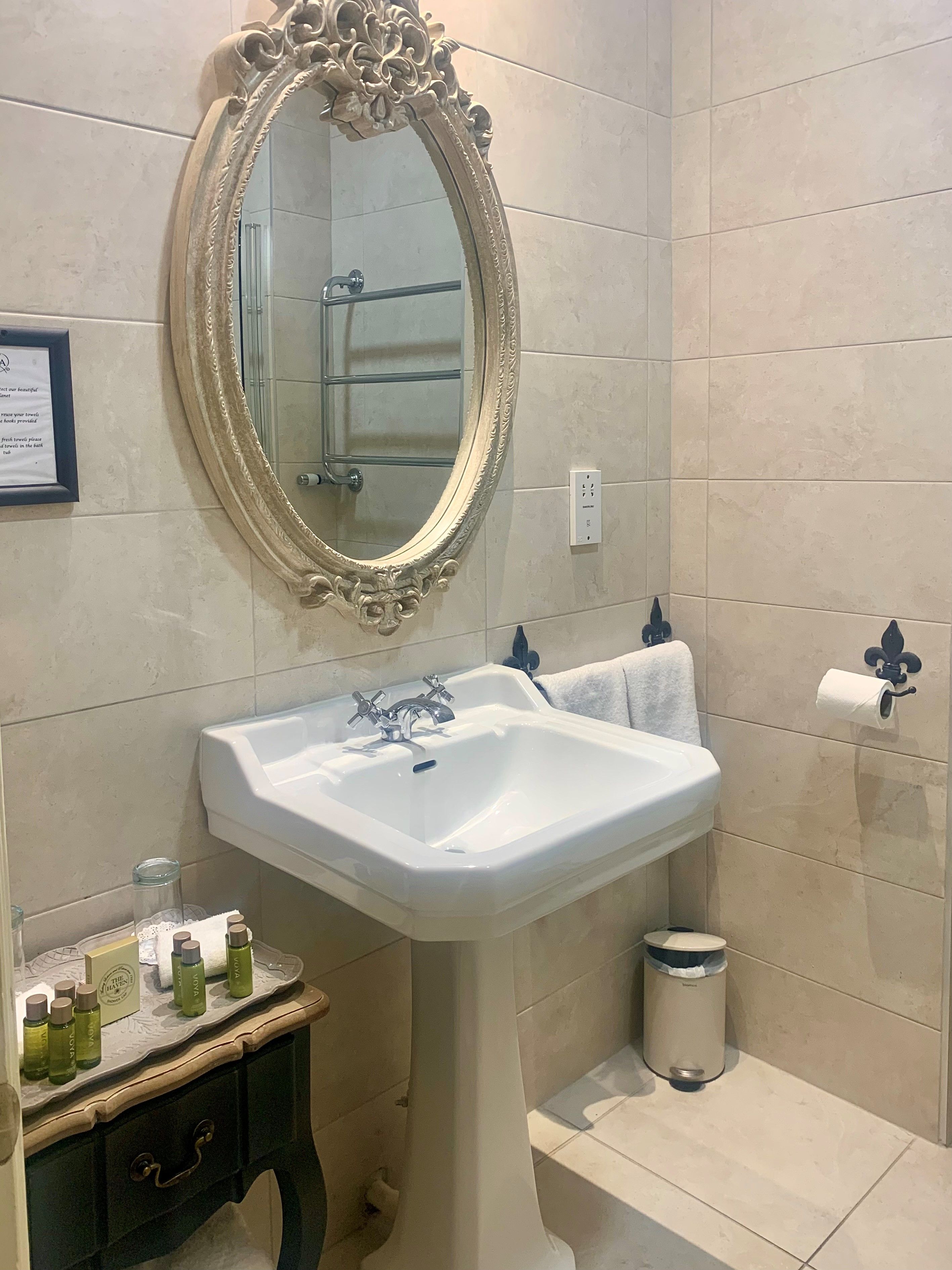 Een badkamer met een wit wastafelmeubel, een decoratieve spiegel, een handdoekrek en toiletartikelen op een ijdelheidsblad.