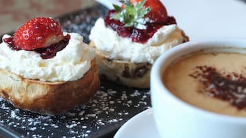 Ein Dessertteller mit zwei Gebäckstücken, bedeckt mit Schlagsahne und Erdbeeren, sowie eine Tasse Kaffee mit Schokoladendrizzle.