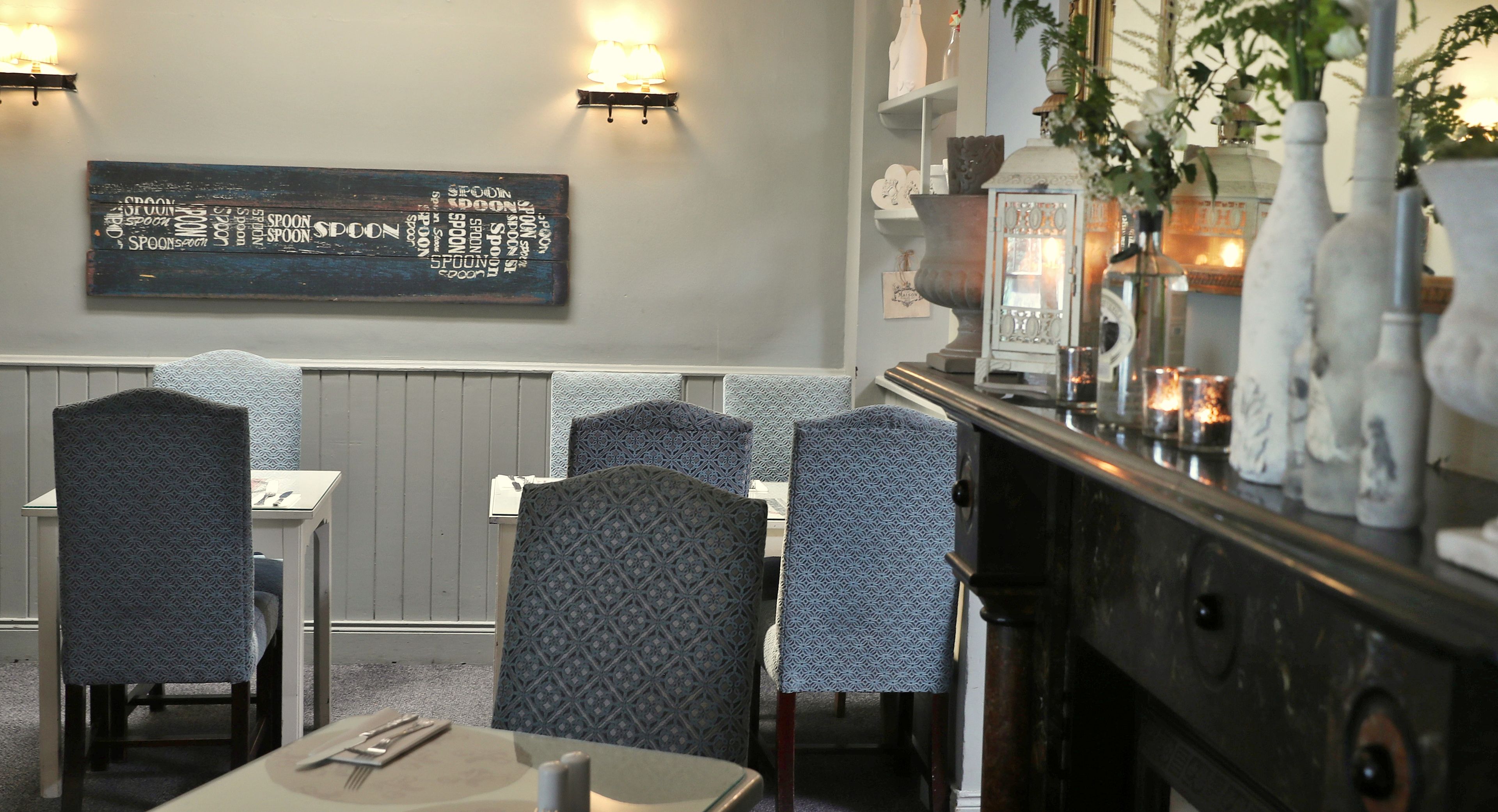 A restaurant interior with patterned chairs, a wall-mounted menu, and decorative lighting.