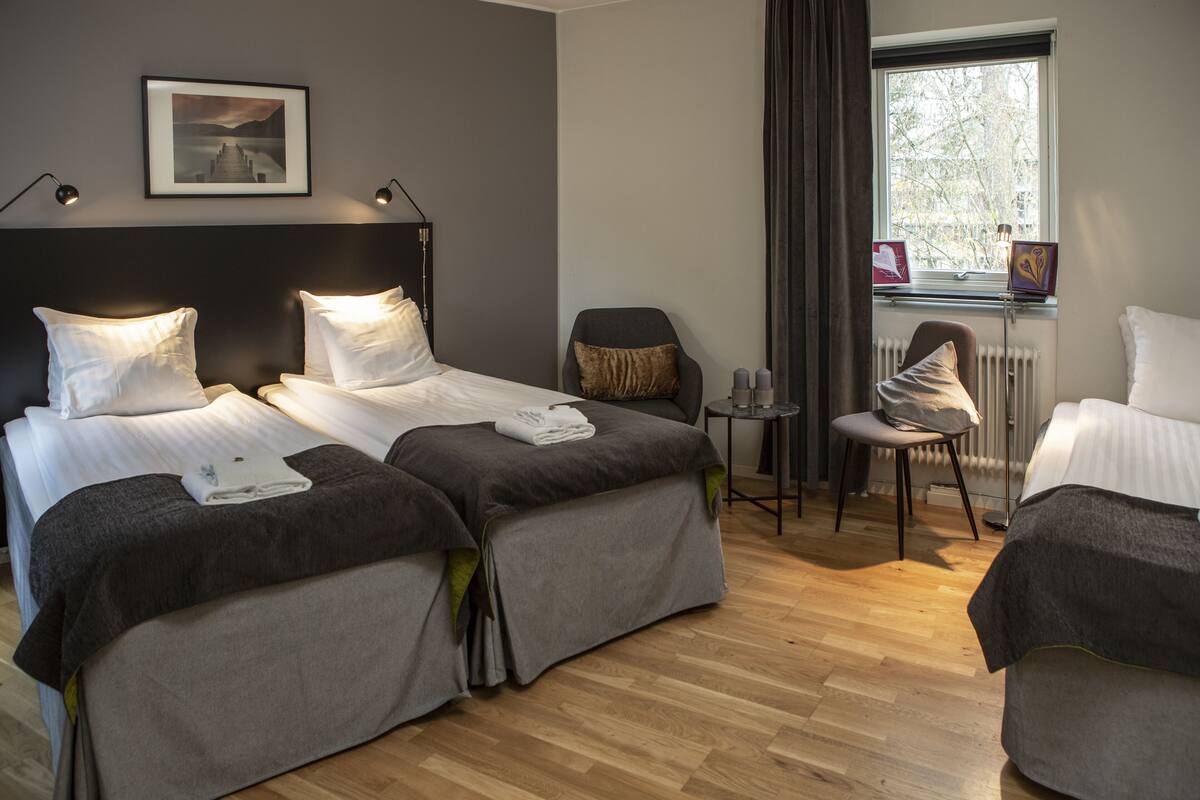 A hotel room with two beds, a chair, a small table, and a window with a view.