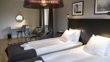A hotel room with two beds, a desk, a chair, and a large lamp.
