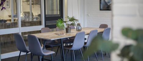 A modern dining area with a wooden table, six grey chairs, and potted plants.
