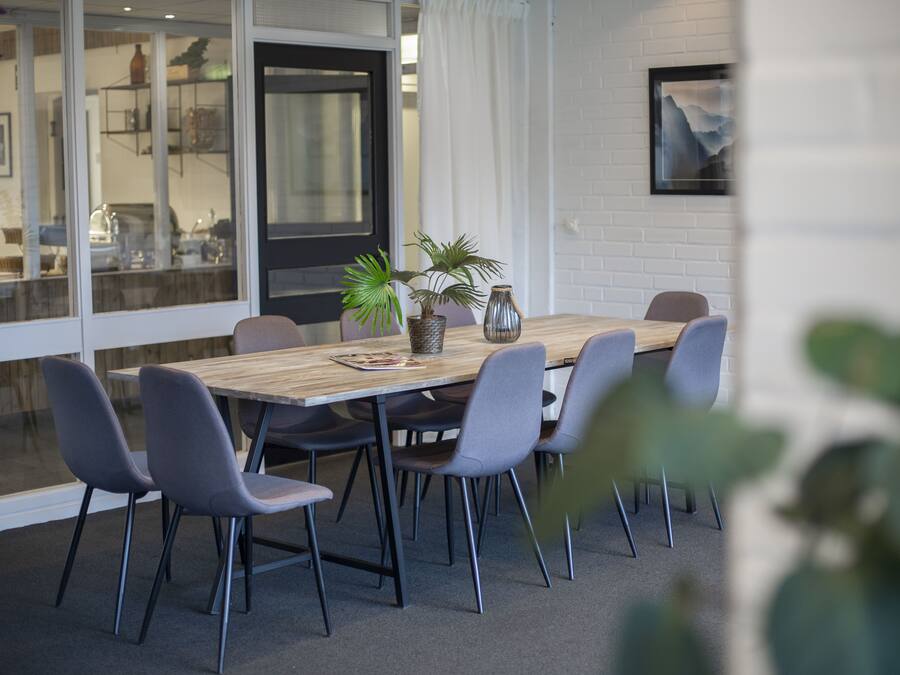 A modern dining area with a wooden table, six grey chairs, and potted plants.