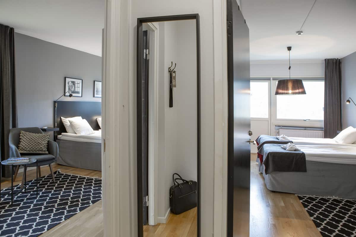A hotel room with a bed, a chair, a small table, and a coat rack.