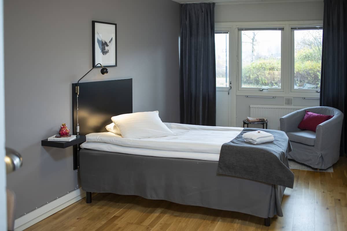 A bedroom with a bed, a chair, a bedside table, a window, and a picture on the wall.