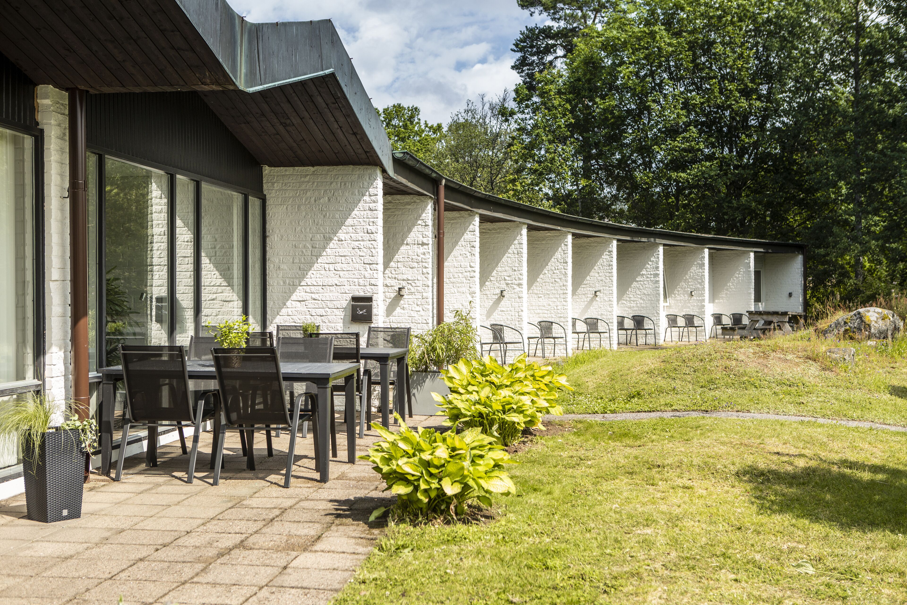 Een terras buiten met een tafel en stoelen, omringd door een witte bakstenen muur en grote ramen.