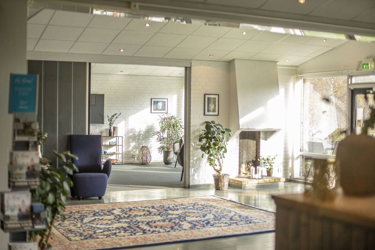 A hotel lobby with a blue armchair, a patterned rug, and potted plants.